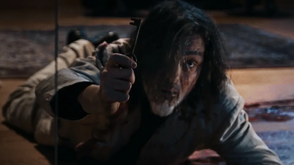 Bloodied man holding up a small metal key